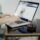 A person typing on a laptop in a stylish home office with a glass of drink nearby.